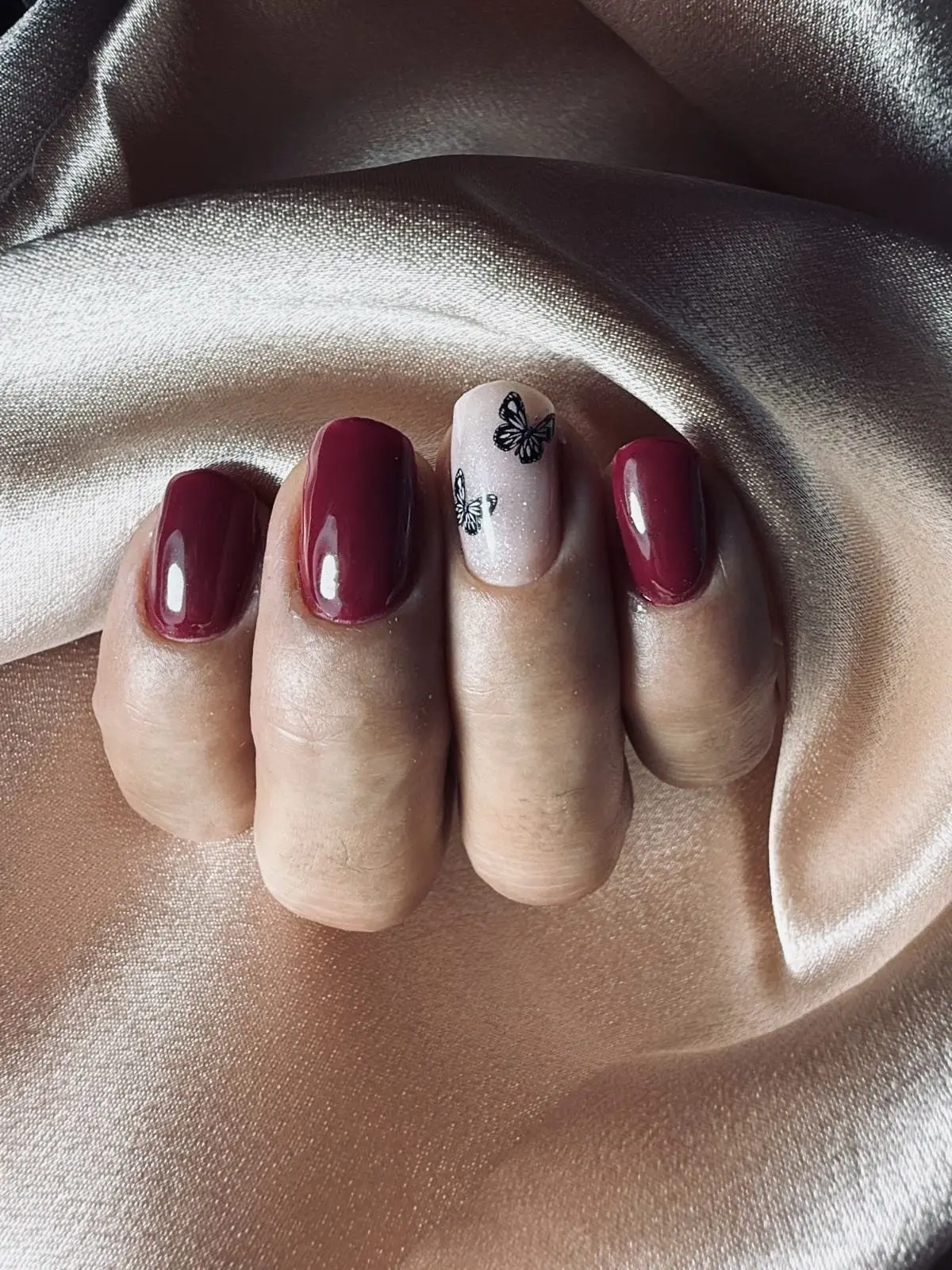 Nail art creativo en Noestyle Baeza: manicura con esmalte burdeos brillante y diseño de mariposas negras